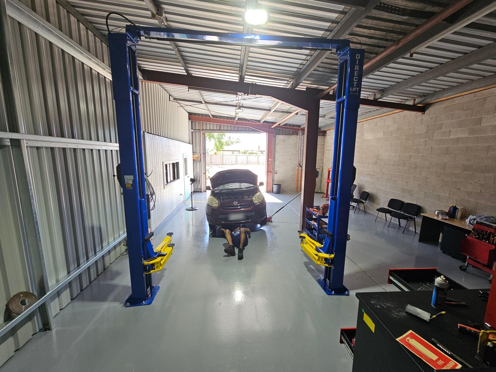 Mechanic working under a Nissan Micra between the posts of a blue two-post hoist in the Townsville Car Care workshop