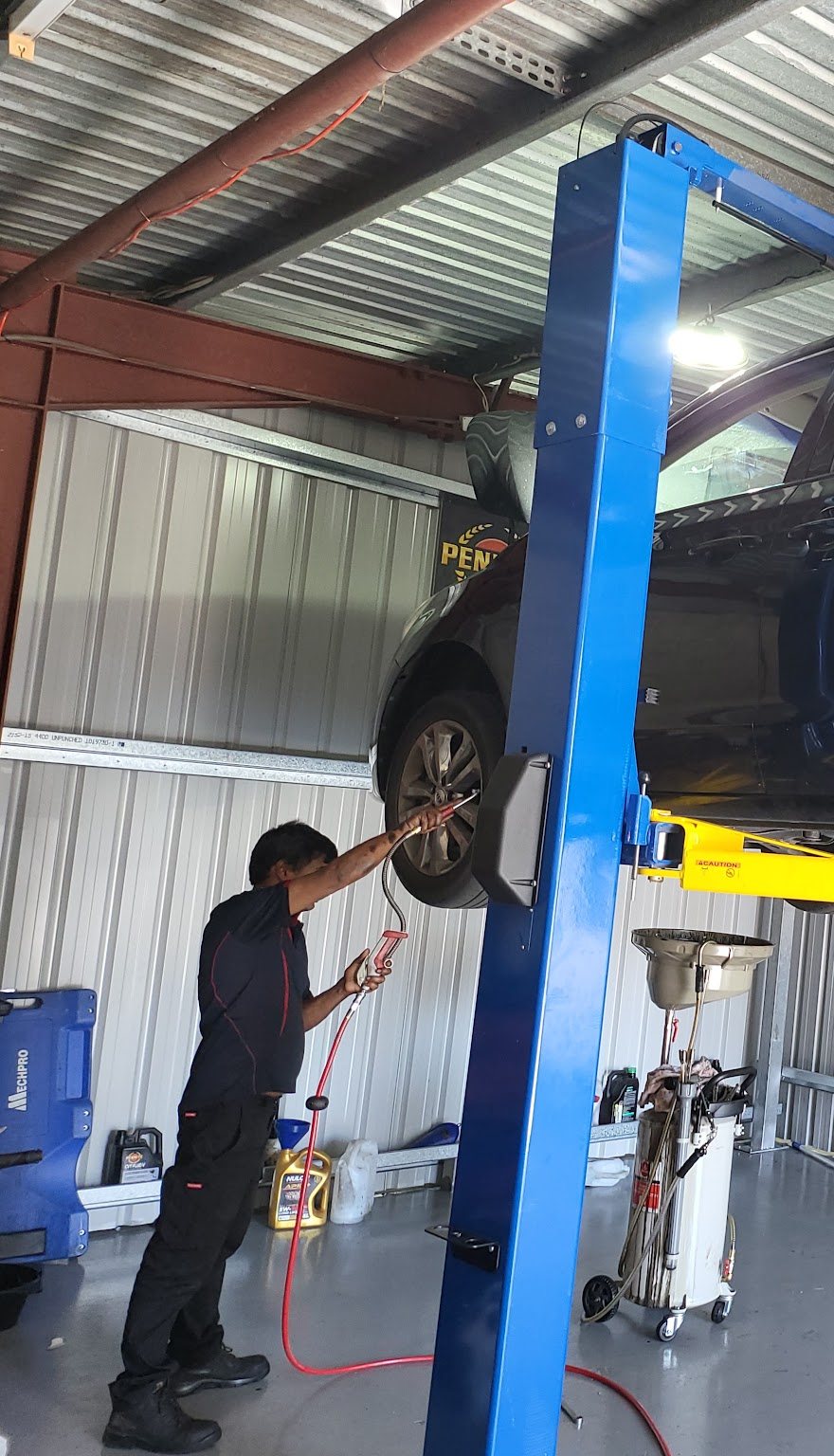 Mechanic using an air tool on a wheel of a raised car beside the blue hoist post