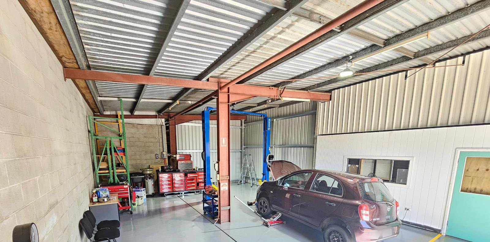 Wide view of the workshop: red tool chests, green racking, a blue two-post hoist and a Nissan Micra being worked on